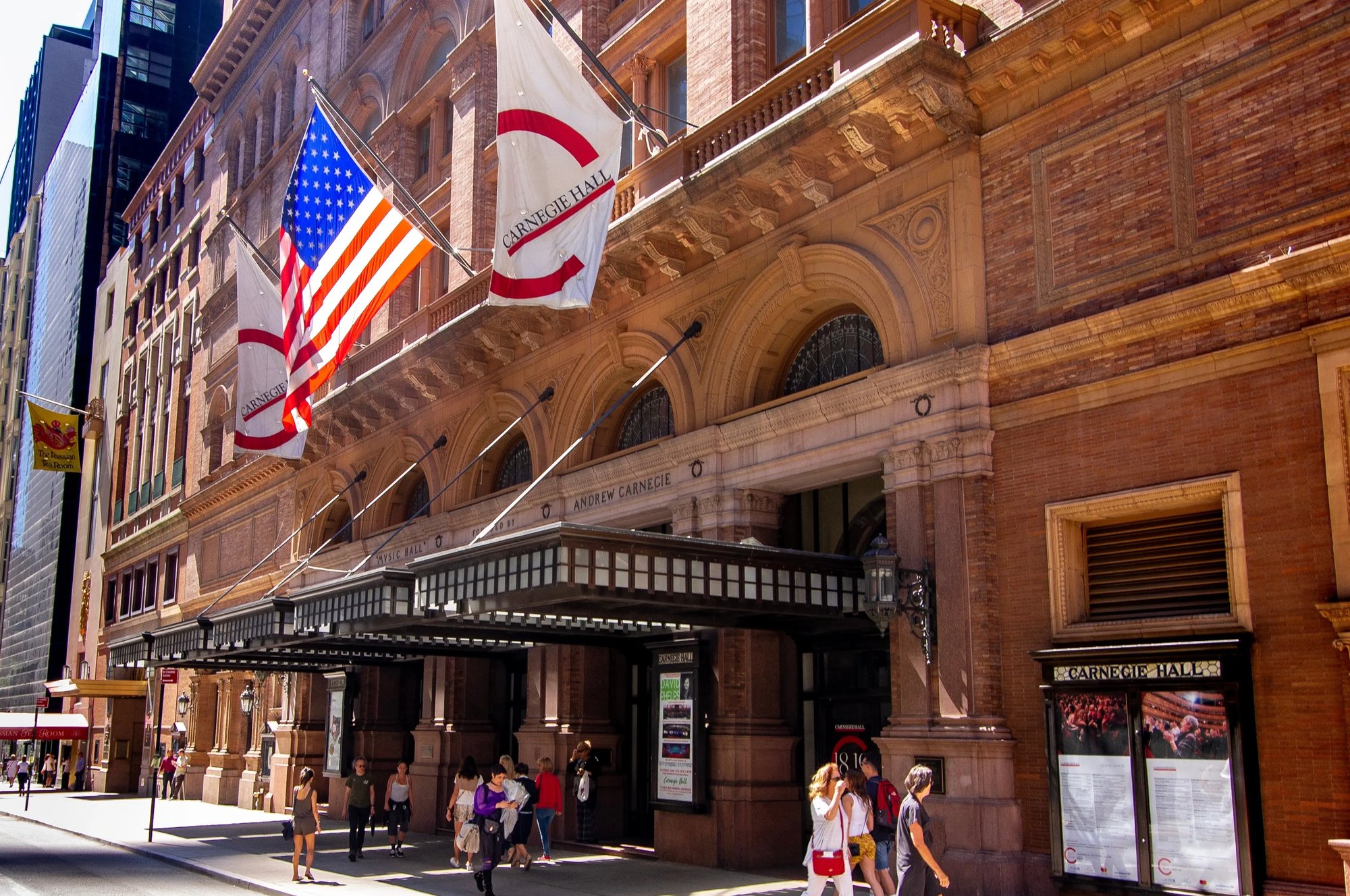 Pedestrians walk in front of covered entrance to brick landmark Carnegie Hall image by RozenskiP